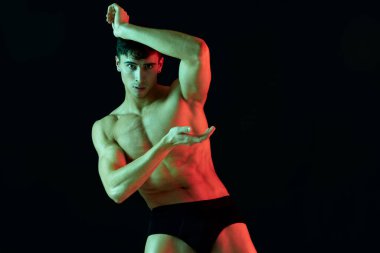 Çıplak erkek sporcu ellerini siyah bir arka plan üzerinde gezdiriyor.