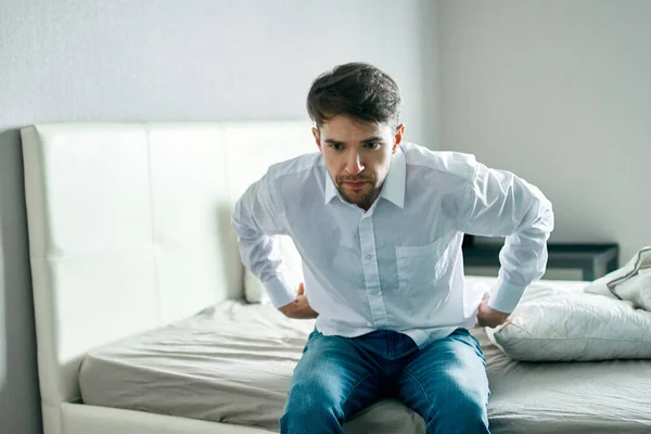 Man in shirt en jeans zit op het bed binnenshuis eenzaamheid — Stockfoto