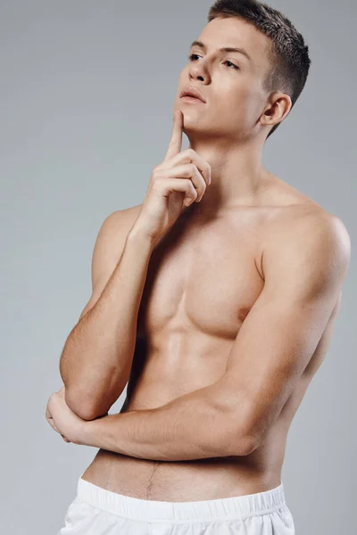 Athlete with a pumped-up torso holds his hand near his face and cubes on his stomach gray background model — Stock Photo, Image