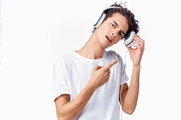 Χαρούμενος σγουρομάλλης τύπος με ακουστικά και λευκό μπλουζάκι ακούει μουσική και κρατά τα χέρια του κοντά στο πρόσωπό του — Φωτογραφία Αρχείου