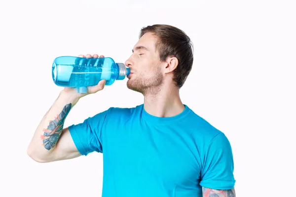 Atleta chico bebe agua de una botella sobre un fondo blanco y una camiseta azul —  Fotos de Stock