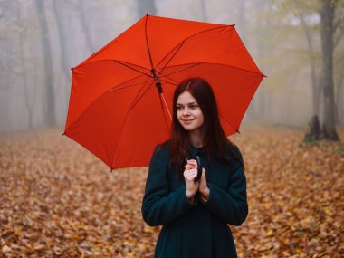 Sonbaharda parkta kırmızı şemsiyeli kadın Sarı yapraklar siste yürüyor