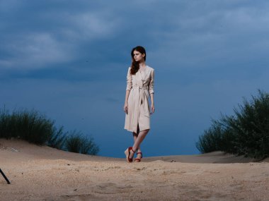 Sundress giymiş bir kadının uzun bir portresi ve kumsalda kırmızı sandaletler.