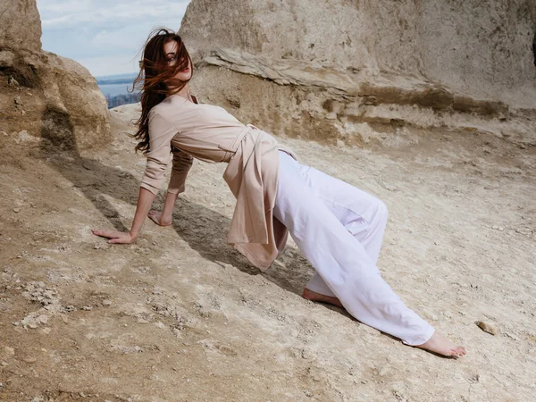 Mujer en pantalones blancos se sienta en la arena cerca de rocas altas —  Fotos de Stock