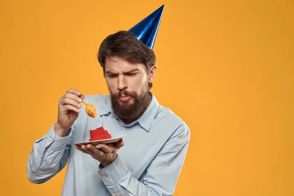 Születésnapi tortával a kezében és sapkában sárga alapon a születésnapján. — Stock Fotó