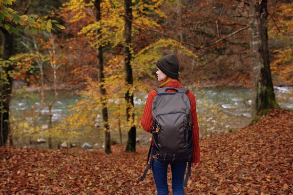 Vrouw in het park in de herfst bij de rivier en een rugzak op haar rug bekijken — Stockfoto