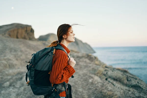 Schöne Modell mit einem Rucksack auf dem Rücken in den Bergen in der Natur in der Nähe des Meeres und hohe Felsen — Stockfoto