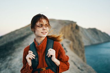 Doğa dağları temiz hava ve sırt çantası ve süveteri olan genç bir gezgin deniz kenarında dinleniyor.