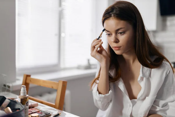 Mulher fazendo maquiagem enquanto se senta na mesa na cozinha e eyeliner fundação — Fotografia de Stock