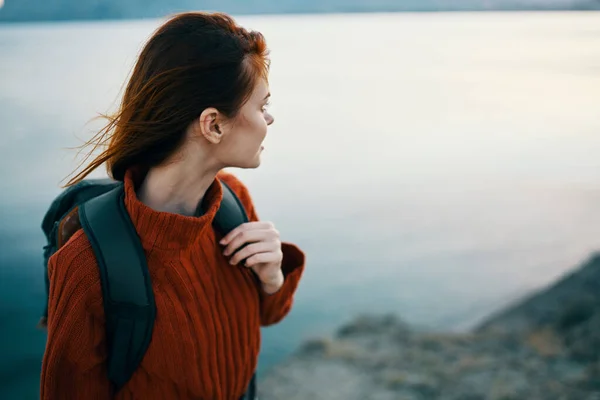 Donna in un maglione vicino al mare in montagna guarda di lato e uno zaino sulla schiena — Foto Stock