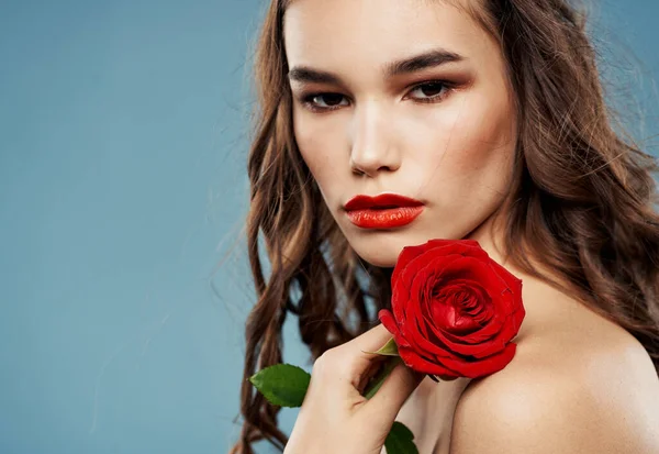 Femme avec une fleur rouge près du visage sur un fond bleu épaules nues ombres sur les paupières — Photo