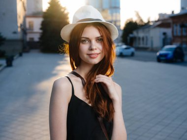 Şehrin caddesinde siyah elbiseli, beyaz şapkalı, kızıl saçlı bir manken.