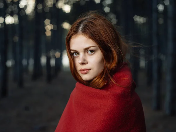 Una mujer con una manta roja sobre sus hombros entre los árboles del bosque —  Fotos de Stock