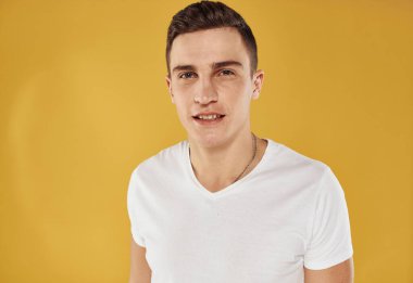 Sarı arka plan modeli üzerinde beyaz tişörtlü genç bir adamın portresi.