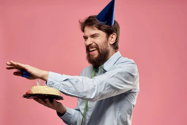 Homme barbu avec langue de gâteau sur un fond rose vue recadrée et une casquette bleue sur sa tête — Photo