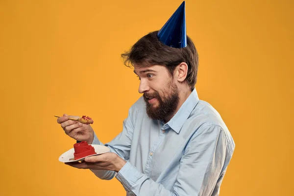 Un hombre con un pastel de cumpleaños en sus manos y con una gorra sobre un fondo amarillo en su cumpleaños —  Fotos de Stock