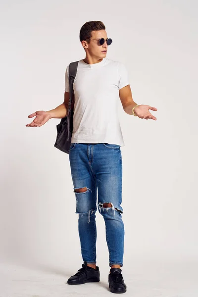 Een man met een rugzak op zijn rug in jeans t-shirt full length sneakers en bril op zijn gezicht — Stockfoto