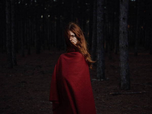 Beautiful woman with a red cape in the black forest at night. High quality photo