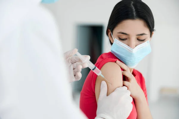 Un médico con una bata blanca hace una inyección en el hombro de un paciente que usa una máscara médica covid —  Fotos de Stock