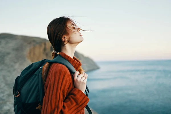 Donna turista con uno zaino in un maglione stanno riposando in montagna vicino al mare e guardando il cielo — Foto Stock