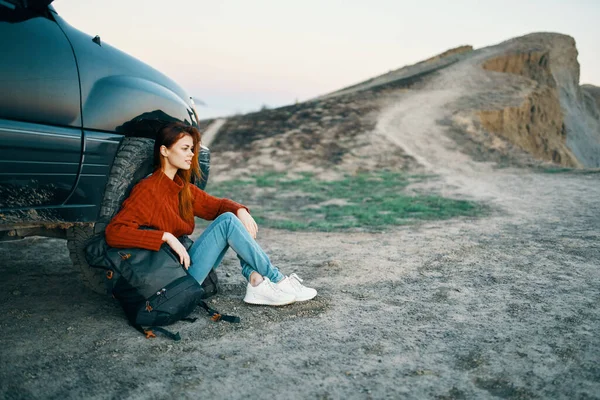 Γυναίκα στα βουνά στην άμμο με ένα σακίδιο κοντά στην κορυφή του αυτοκινήτου άποψη — Φωτογραφία Αρχείου