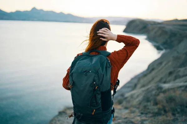 a traveler with a backpack on her back looks at the sea in the distant mountains landscape ocean clear water