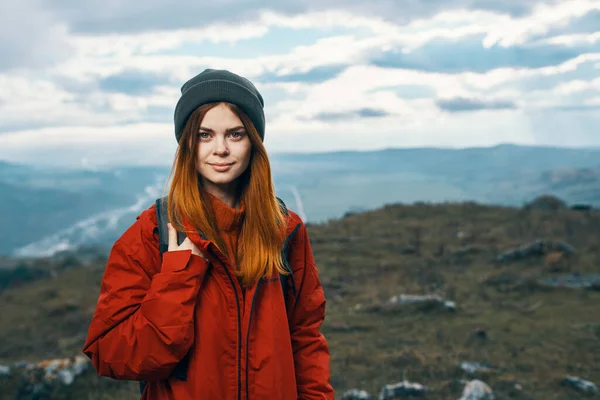 Femme heureuse dans une veste rouge avec un sac à dos et dans un chapeau montagnes en arrière-plan air frais — Photo