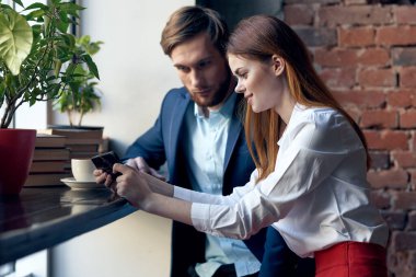 İş arkadaşı erkek ve kadın bir kafede oturmuş telefon konuşmaları yapıyorlar.