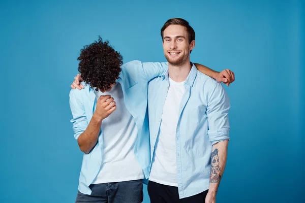 Mladí muži v identické košile objímání na modrém pozadí nejlepší přátelé zábava — Stock fotografie