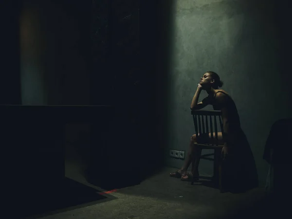 Femme assise sur une chaise dans une pièce sombre chute lumière solitude émotions bouleversé dépression — Photo