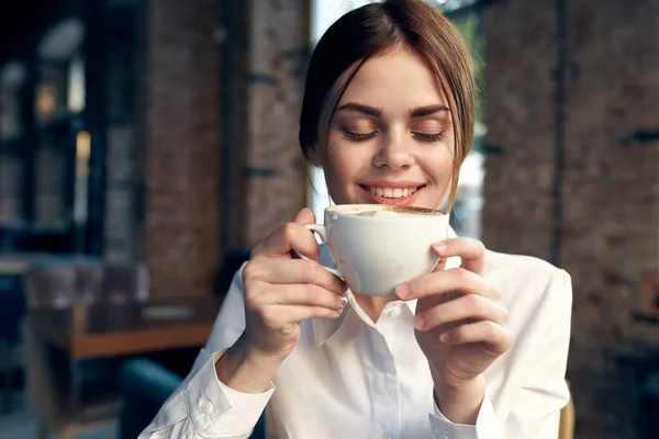 Mulher de negócios bonita na camisa branca senta-se em um café com uma xícara de café — Fotografia de Stock