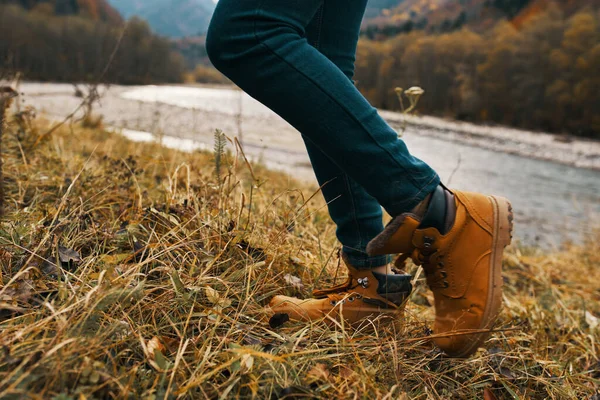 Mulheres pés jeans sapatos grama seca outono rio montanhas à distância — Fotografia de Stock