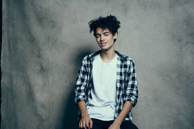 Neşeli adam, kıvırcık saçlı, ekose gömlekli stüdyo gri arka planlı.