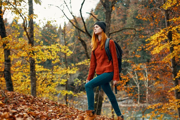 Glückliche Wanderin mit Rucksack auf dem Rücken in Jeans und rotem Pullover in der herbstlichen Waldparklandschaft — Stockfoto