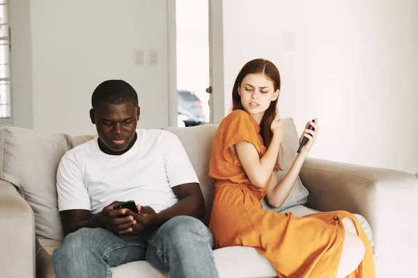 Homme africain avec téléphone portable et femme offensée assis sur le canapé à l'intérieur — Photo