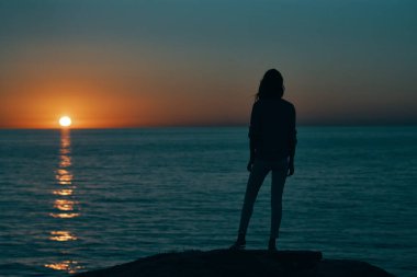 Gün batımında deniz siluetinde bir kadın Sahilde ve gökyüzünde