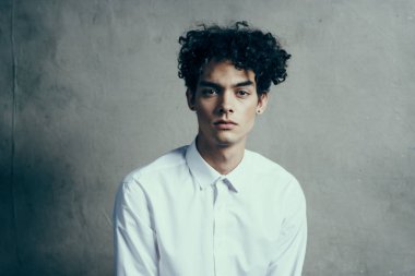 Yakışıklı, kıvırcık saçlı, beyaz gömlekli, modern görünüyor.