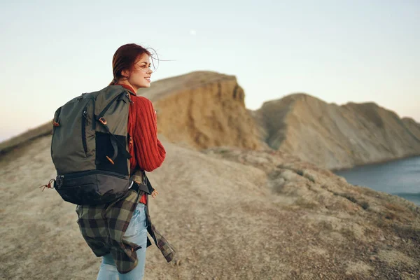Schöne Frau in den Bergen in der Natur mit einem Rucksack auf dem Rücken in Meeresnähe — Stockfoto