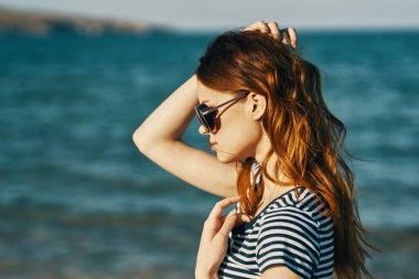 Deniz kenarındaki dağlarda güneş gözlüklü kızıl saçlı bir kadının portresi ve kahkahalar atan bir seyahat. 