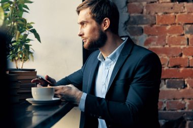 Takım elbiseli bir iş adamı bir kafede bir fincan kahveyle masada oturuyor.