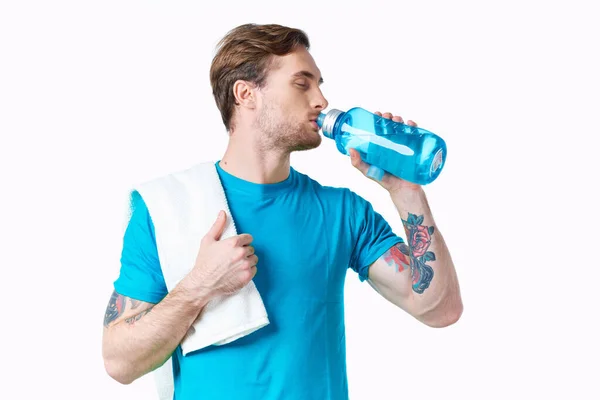 Man athlete drinks water from a bottle on a white background and a towel on his shoulder — Stock Photo, Image