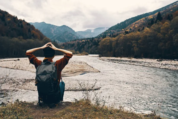 여자 여행자는 강둑에 앉아 멀리 뒤에 보이는 산의 경관을 감상 한다 — 스톡 사진