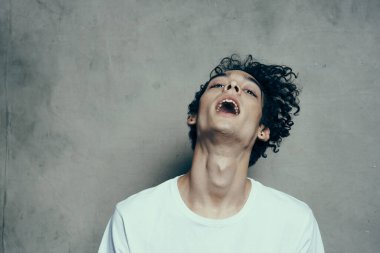 Kıvırcık saçlı neşeli adam gri arka plan fotostudio modelinde başını yana eğiyor.