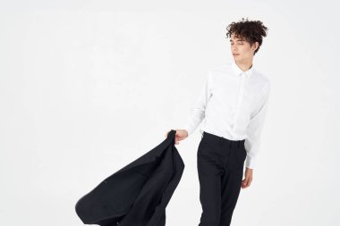 Kıvırcık saçlı ve klasik takım elbiseli genç adam elinde bir ceket tutuyor. Moda tarzı fotoğraf stüdyosu modeli.