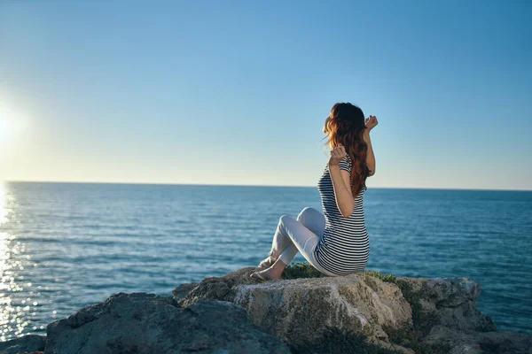 Happy woman on a rock near the sea sunset blue sky and clear water — Stock Photo, Image