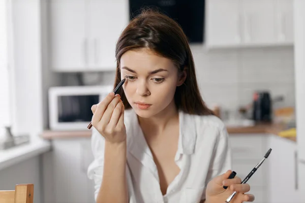 Mujer en la cocina haciendo maquillaje con lápiz de ojos en la mano —  Fotos de Stock