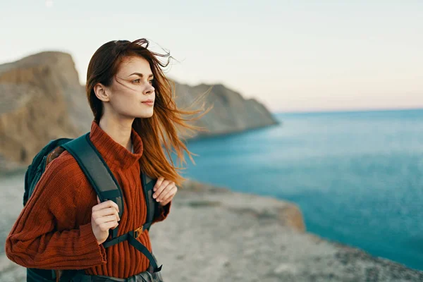 Piękna kobieta w swetrze z plecakiem na plecach w pobliżu morza w górach w przyrodzie — Zdjęcie stockowe