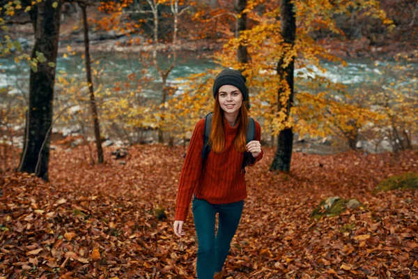 Ein Reisender in rotem Pullover und Hut spaziert durch den herbstlichen Wald in der Nähe eines Gebirgsflusses — Stockfoto