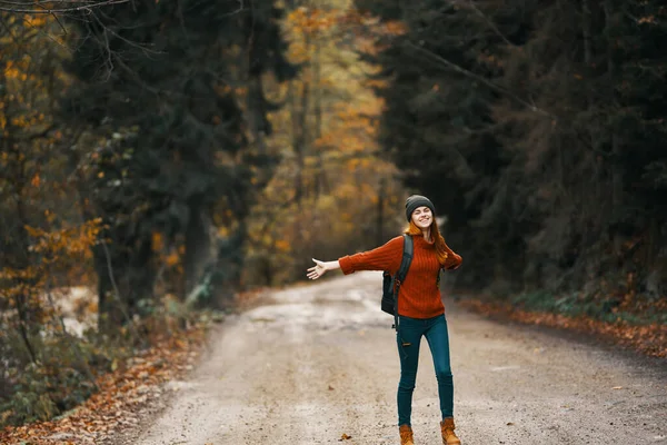 Mulher feliz caminhante com mochila caminha na estrada na floresta de outono — Fotografia de Stock