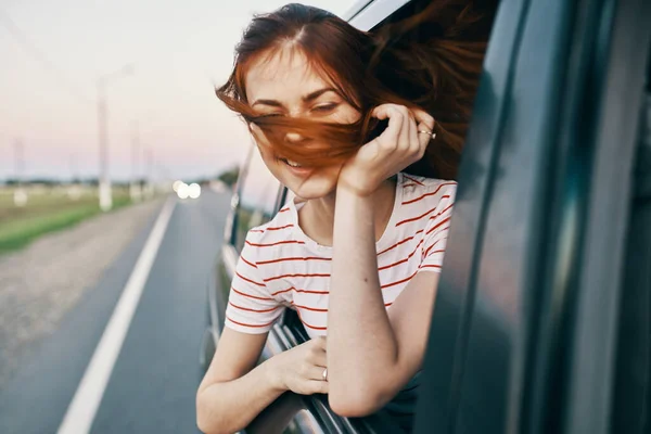 Mujer enérgica camiseta de pelo rojo asomándose por la ventana abierta del coche en el viaje por carretera — Foto de Stock